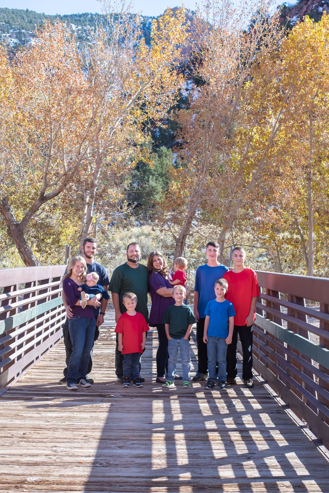 Family of 11 standing on a bridge and smiling with fall leaves in the background-Bethany Allen Photography