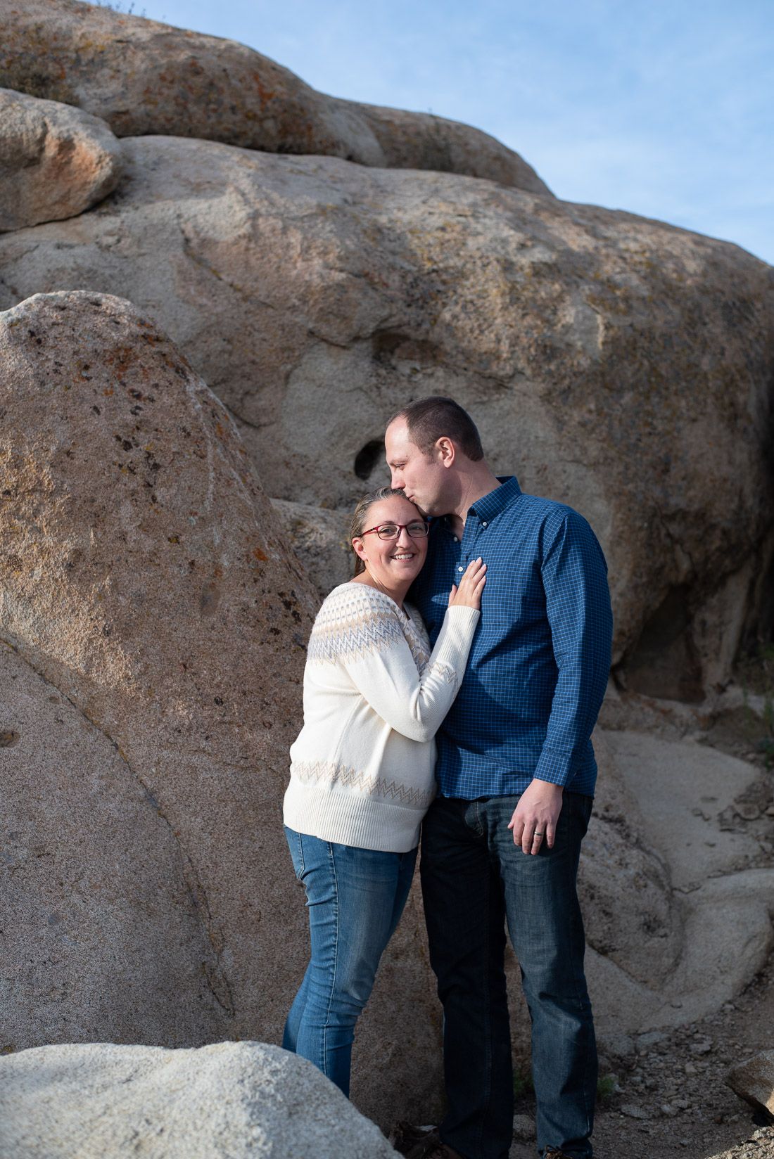 Husband kisses wife's hair while she smiles at the camera-Bethany Allen Photography