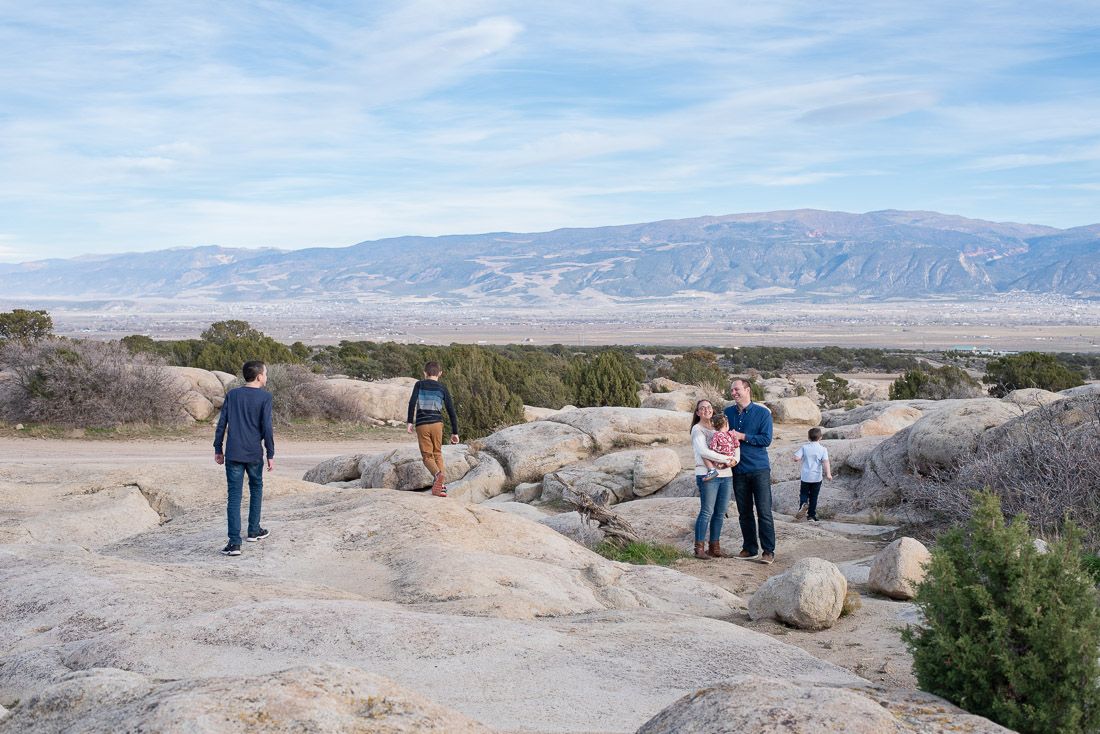 Mom and Dad hold toddler while  older kids run around and play-Bethany Allen-Utah Family Photographer