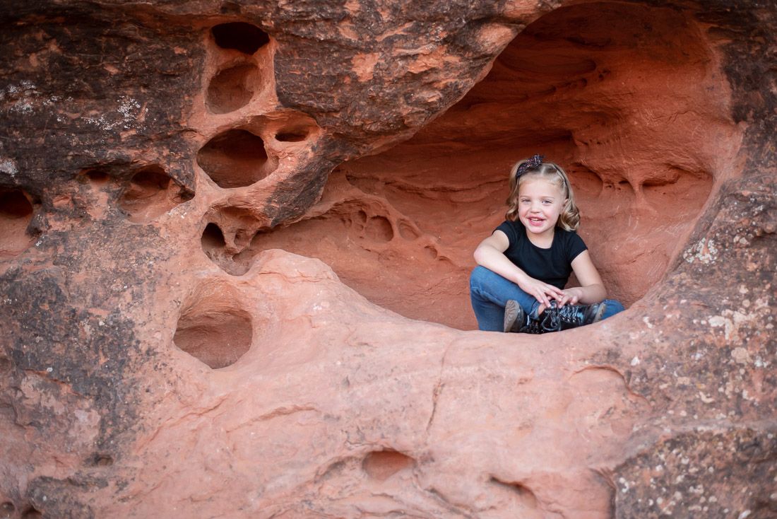 Young girl sitting cross-legged in a hole in red rocks-Bethany Allen