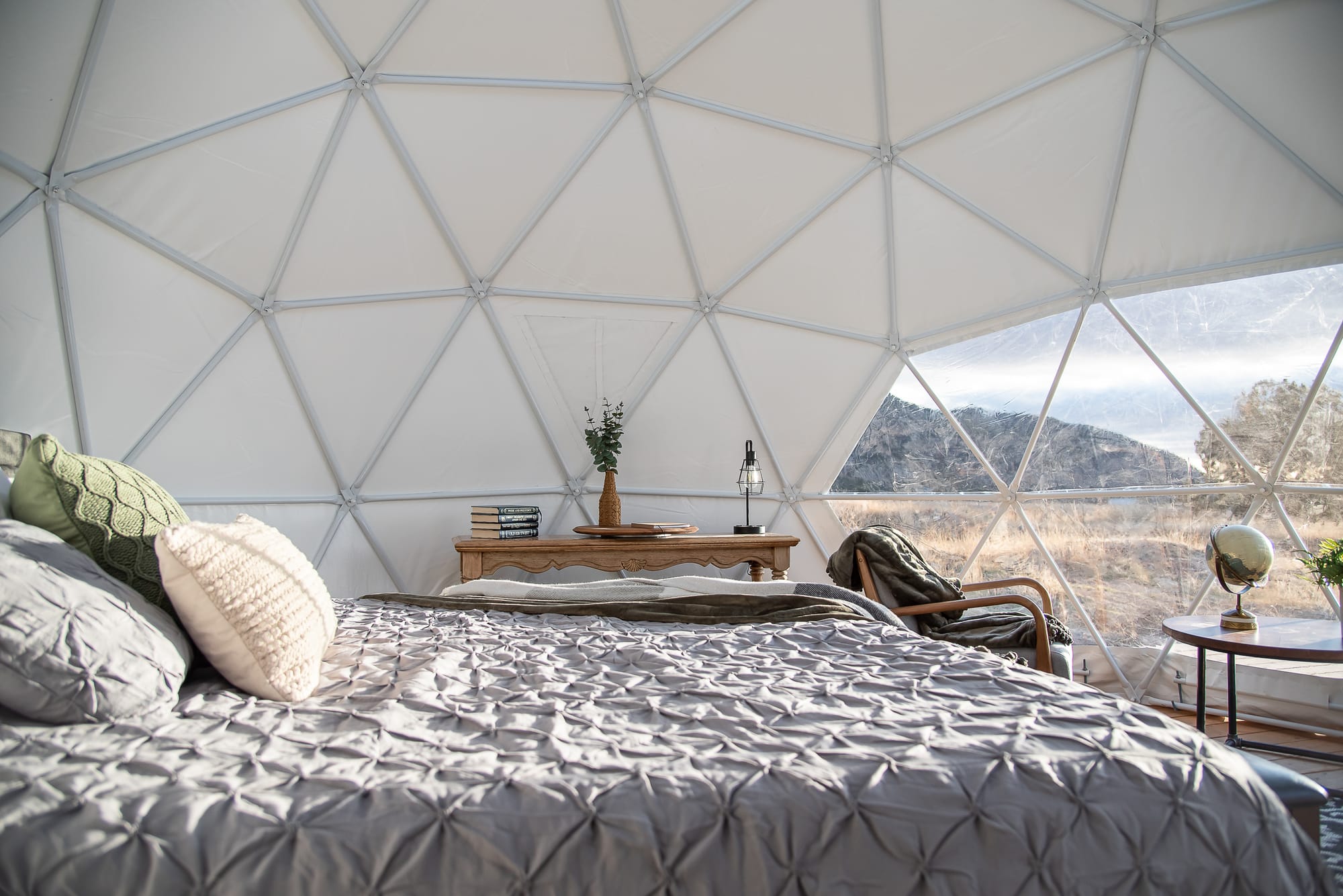 Wide angle shot of the interior of a glamping dome with bed and side table